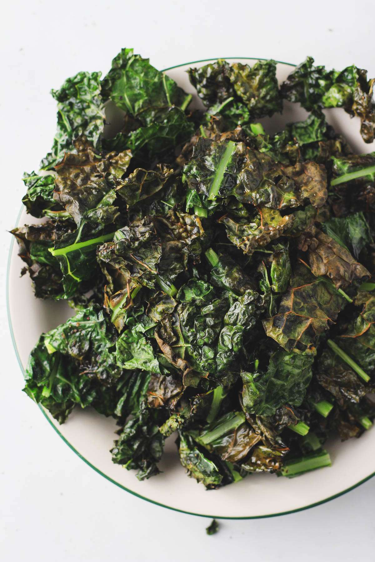 A green rimmed white plate topped with air fryer kale chips on a white counter.