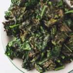 Crispy, vegan air fryer kale chips on a white plate with a green rim.