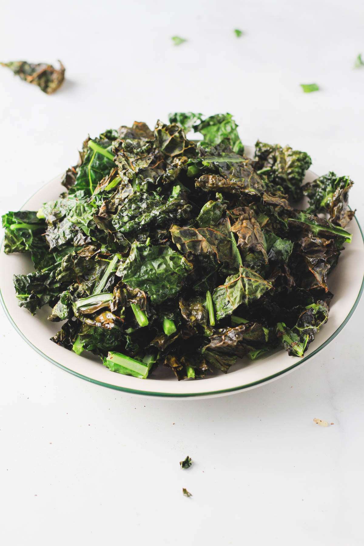 Vegan air fryer kale chips on a white plate with a green rim from the side.