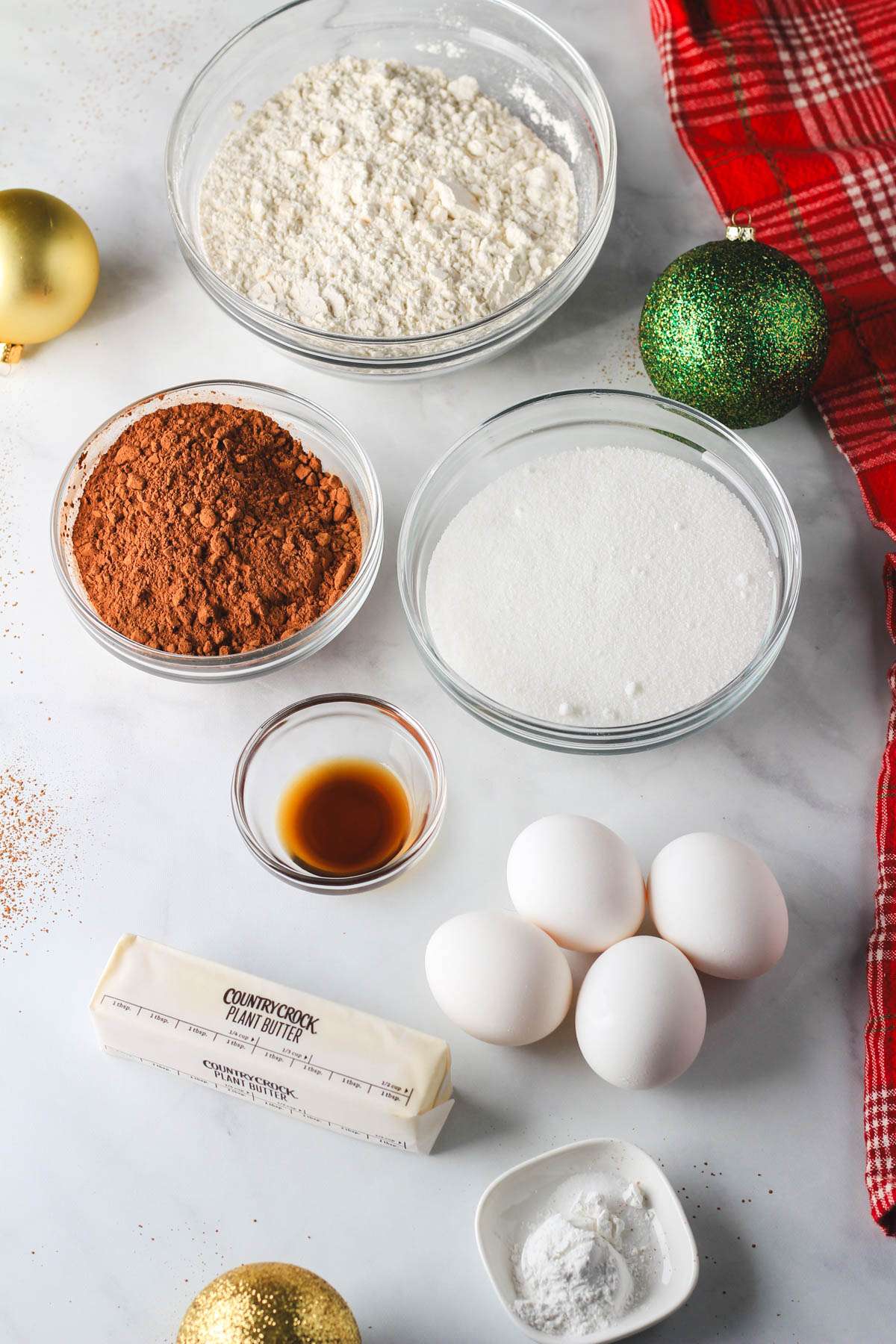 Ingredients for chocolate crinkle cookies on a white counter with a red towel to the right.
