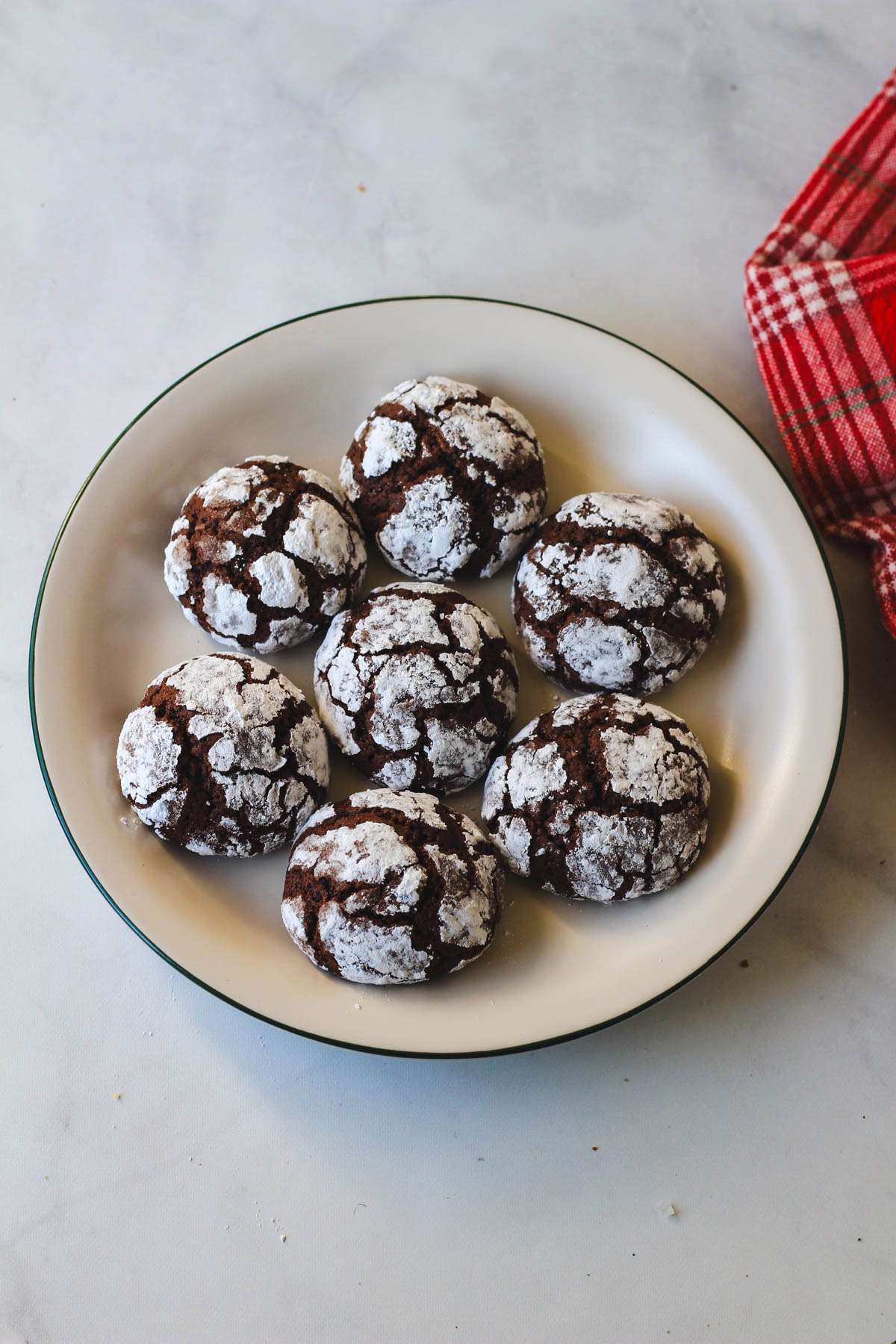 A small white plate with a green rim topped with baked dairy-free chocolate crinkle cookies.