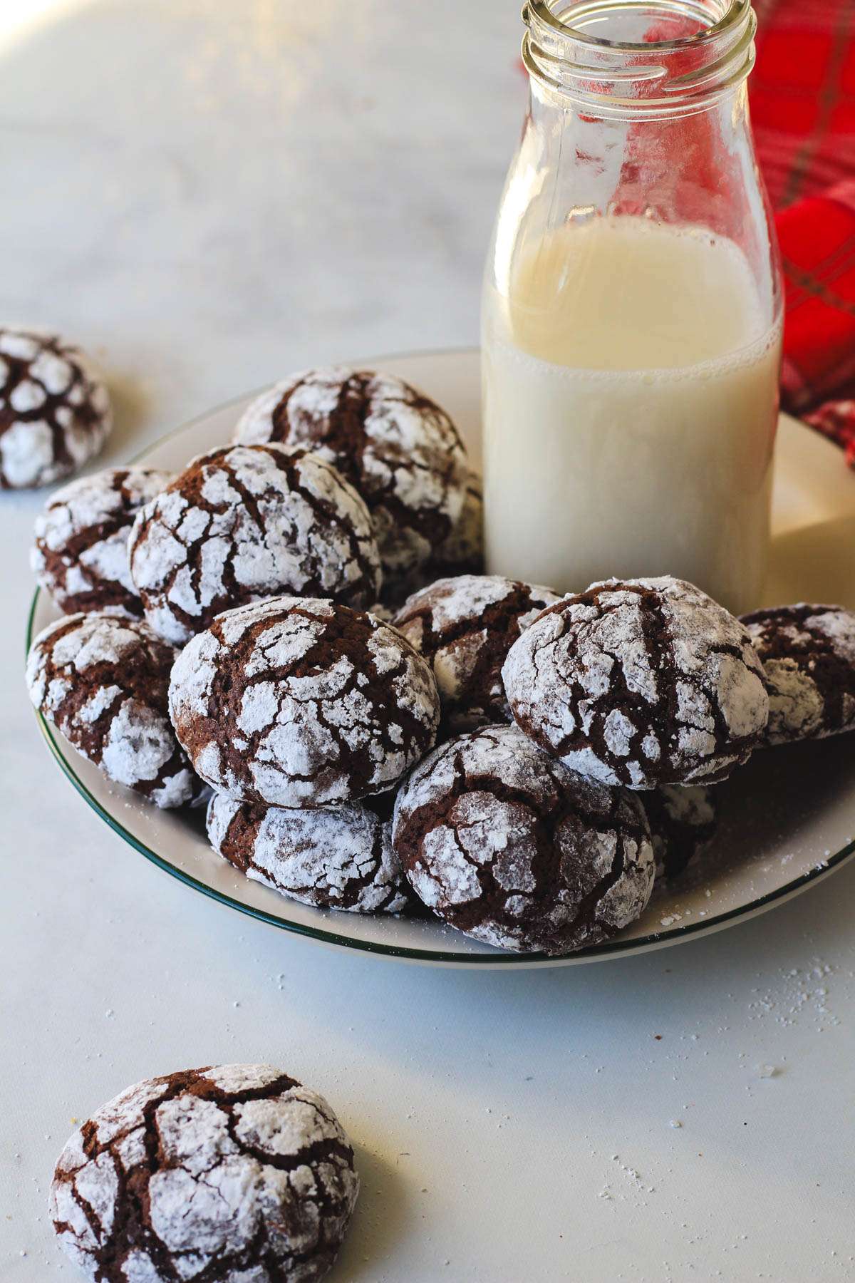 A small white plate with a green rim topped with chocolate crinkle cookies and a bottle of oat milk.