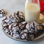 A plate of chocolate crinkle cookies with a bottle of oat milk on a white counter.