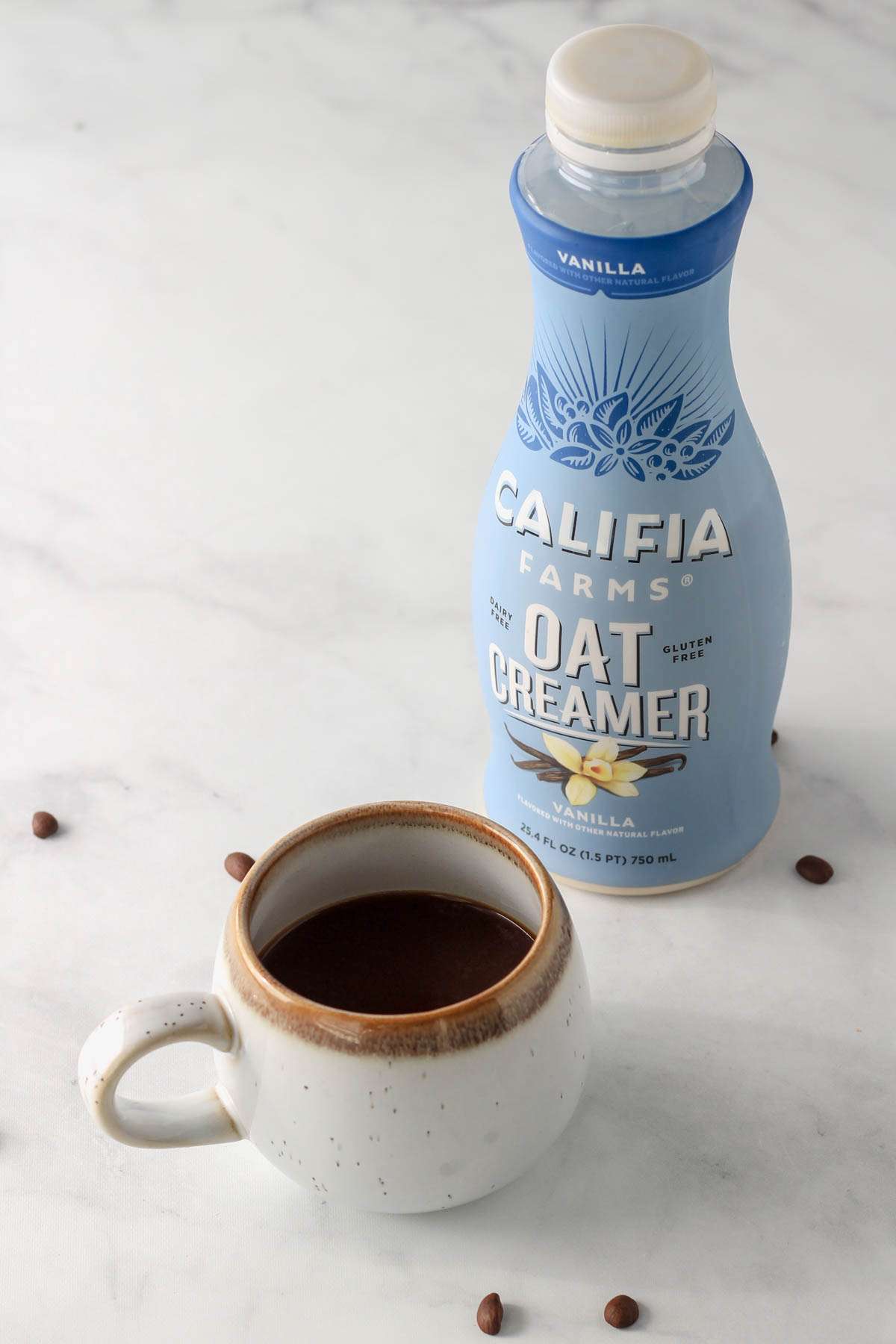 A coffee cup in front of a blue bottle of oat milk coffee creamer.