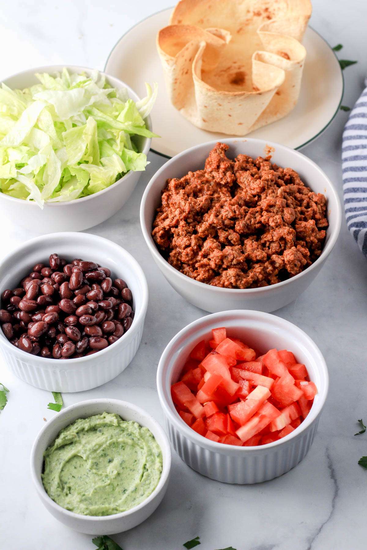 Various white bowls filled with different toppings for the taco salad.