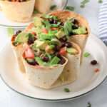 From the side, a dairy-free taco salad in a baked flour tortilla on a white plate with a green rim.