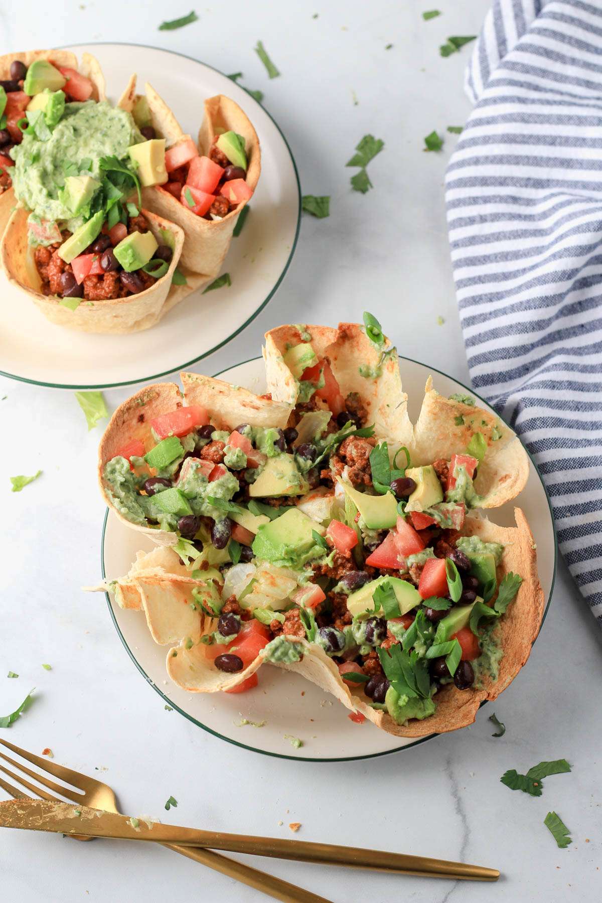 Dairy-free taco salad in a baked tortilla shell with lettuce, taco meat, beans, tomatoes, avocado, cilantro, green onion, and an avocado dressing.
