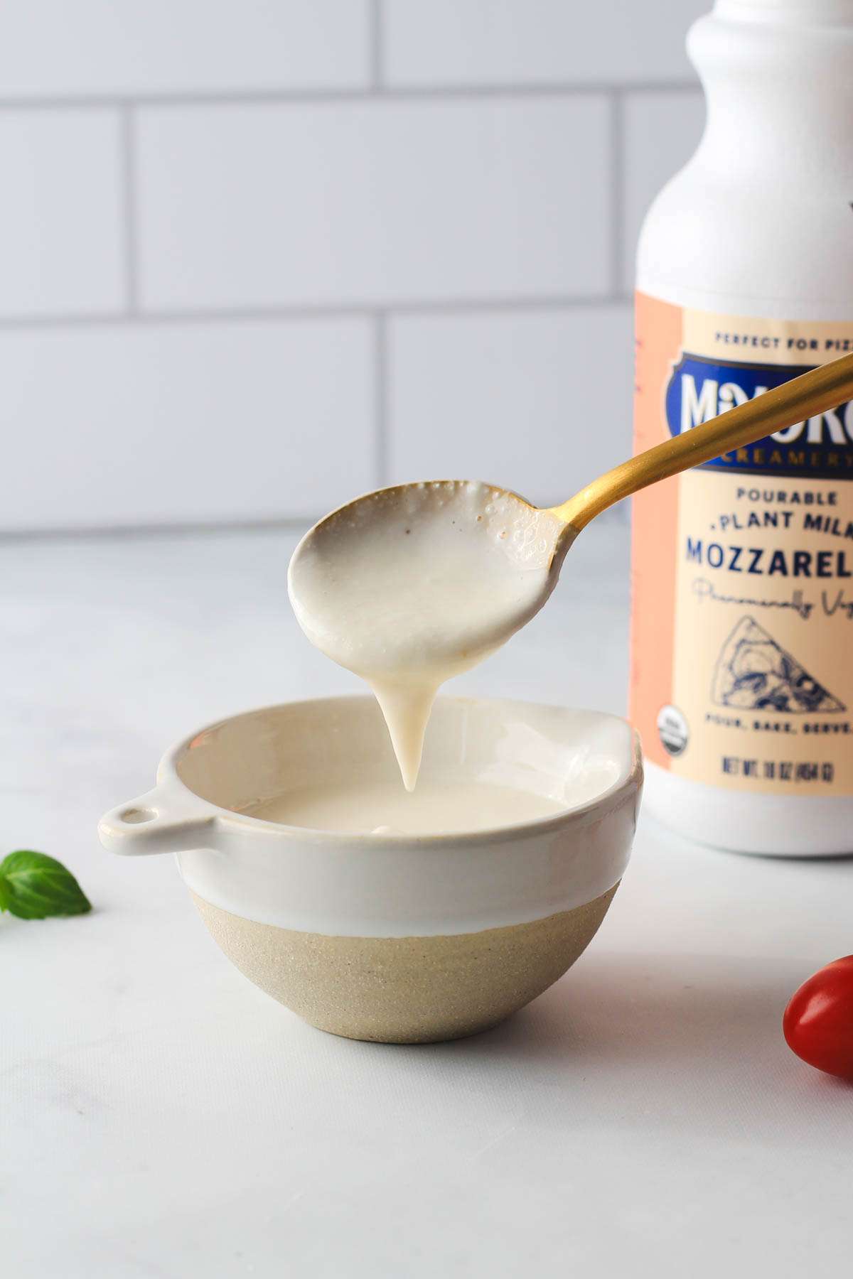 A gold spoon scooping Miyoko's plant cheese out of a white and cream bowl.