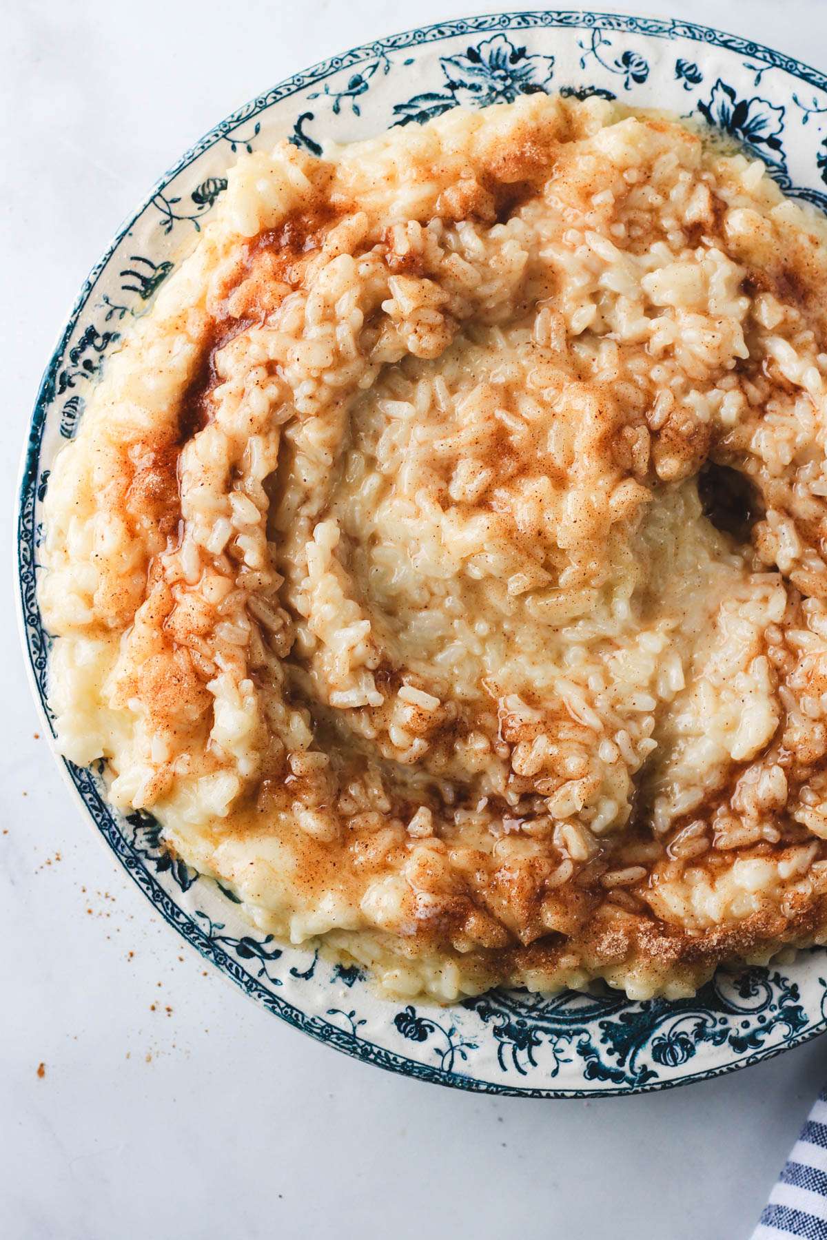 A blue and white rimmed bowl with vegan rice pudding topped with cinnamon sugar and melty vegan butter.