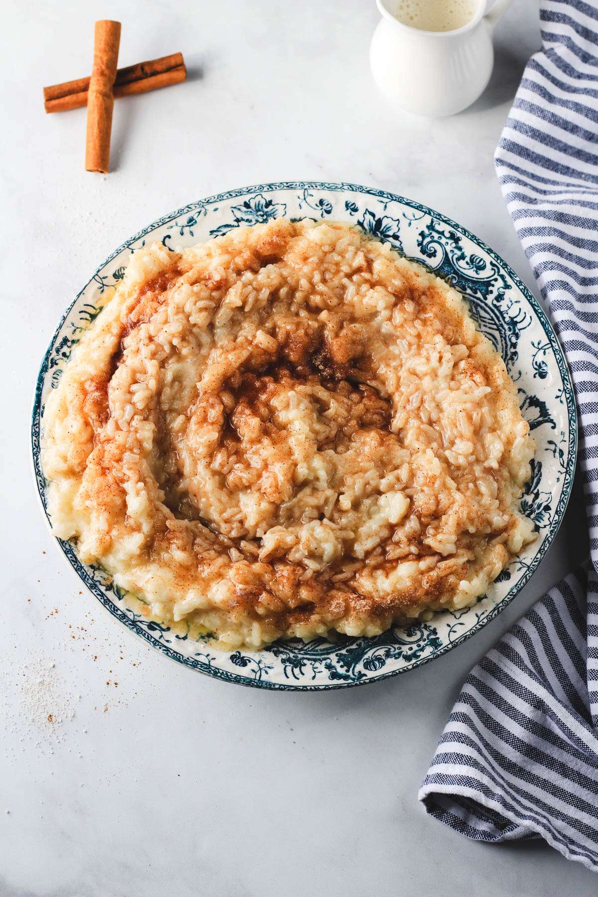A blue and white rimmed bowl of oat milk rice pudding topped with cinnamon sugar on a white counter.
