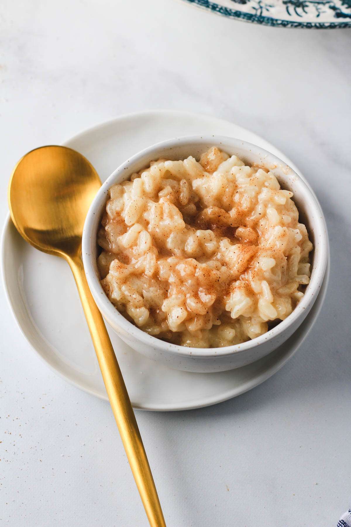A small white bowl filled with Gram's sweet rice on a small white plate with a gold spoon to the left.