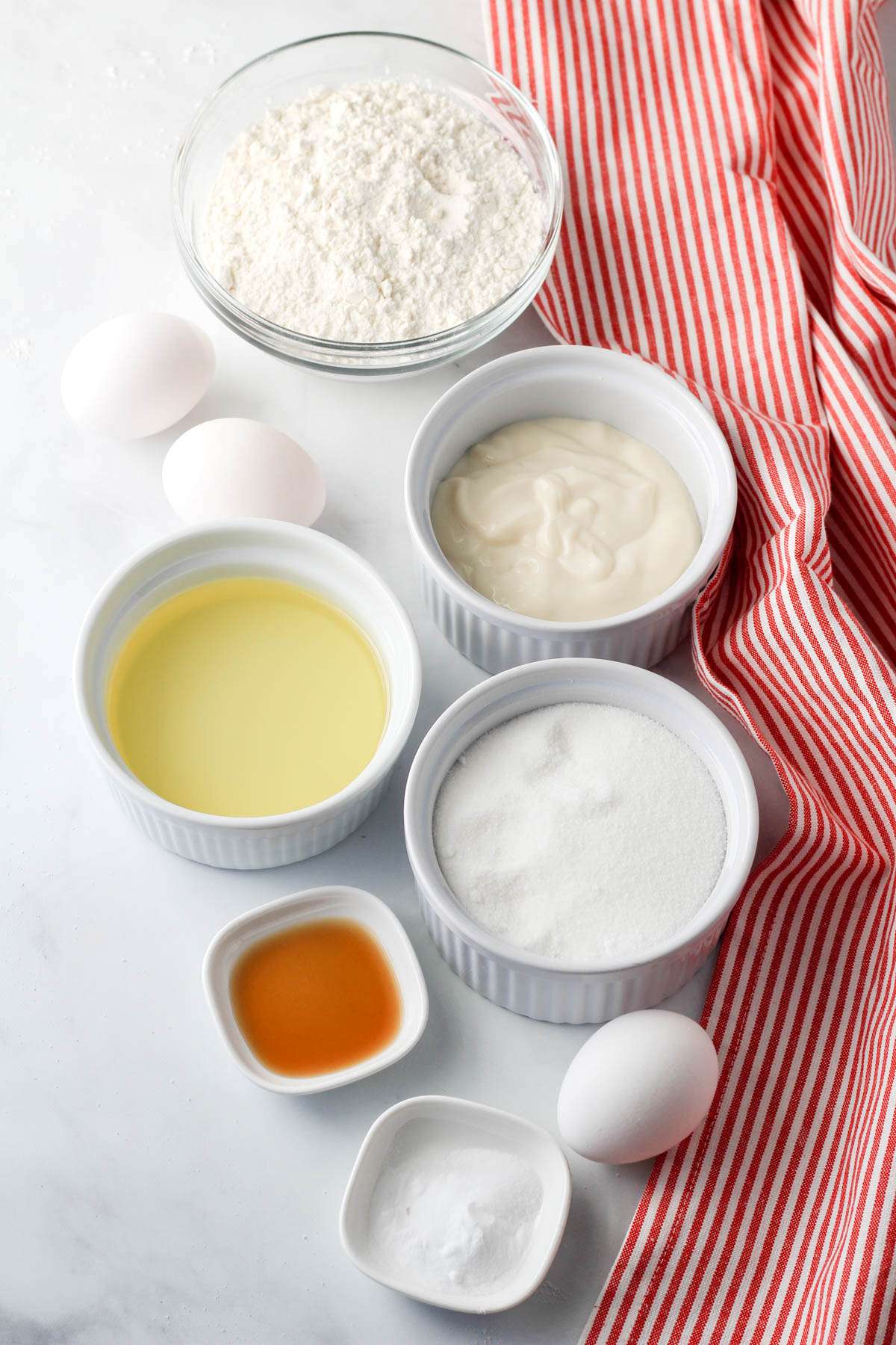 Ingredients for dairy-free yogurt cake on a white counter with a red and white dish towel to the right.