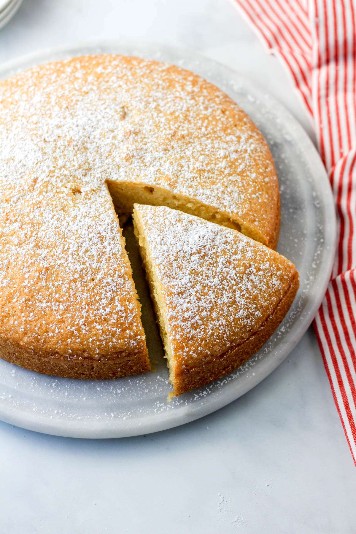 A large slice of dairy-free yogurt cake on a marble plate with the rest of the cake.