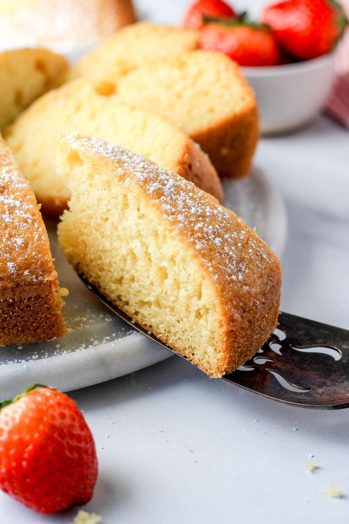 A cake server with a slice of dairy-free yogurt cake pulled off the marble cake stand.
