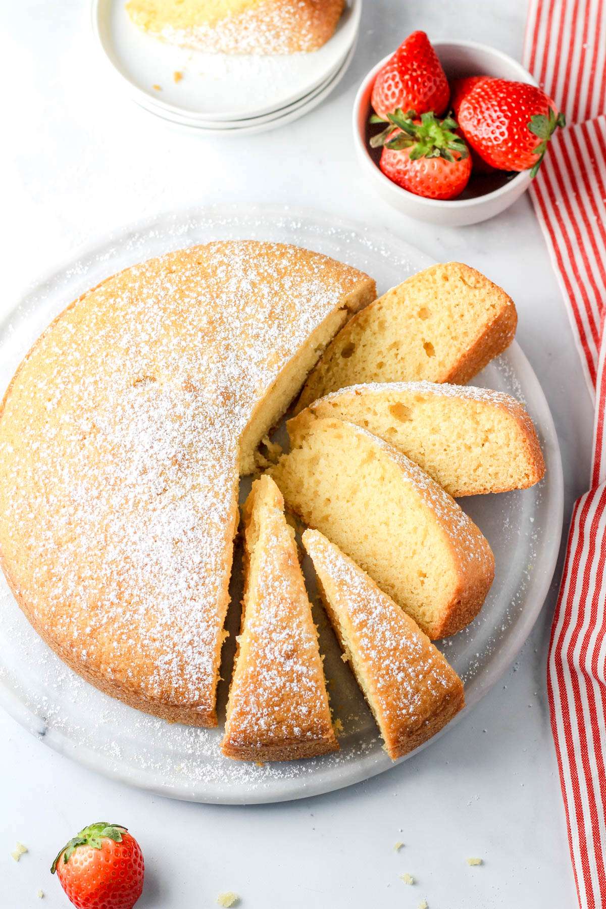 A top down photo of a dairy-free yogurt cake sliced on the right side of the plate with various angles of the slices being shown.