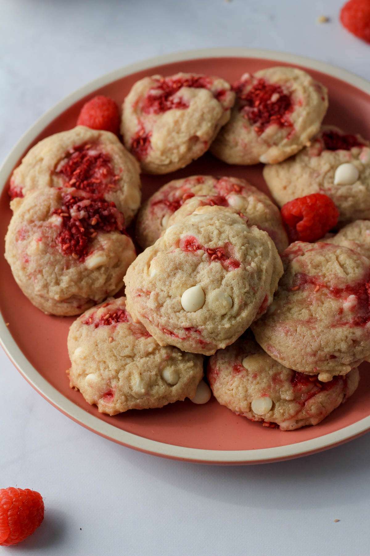 A pile of baked raspberry white chocolate chip cookies on a pink plate.