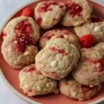 A pink plate topped with white chocolate chip cookies made with fresh raspberries.
