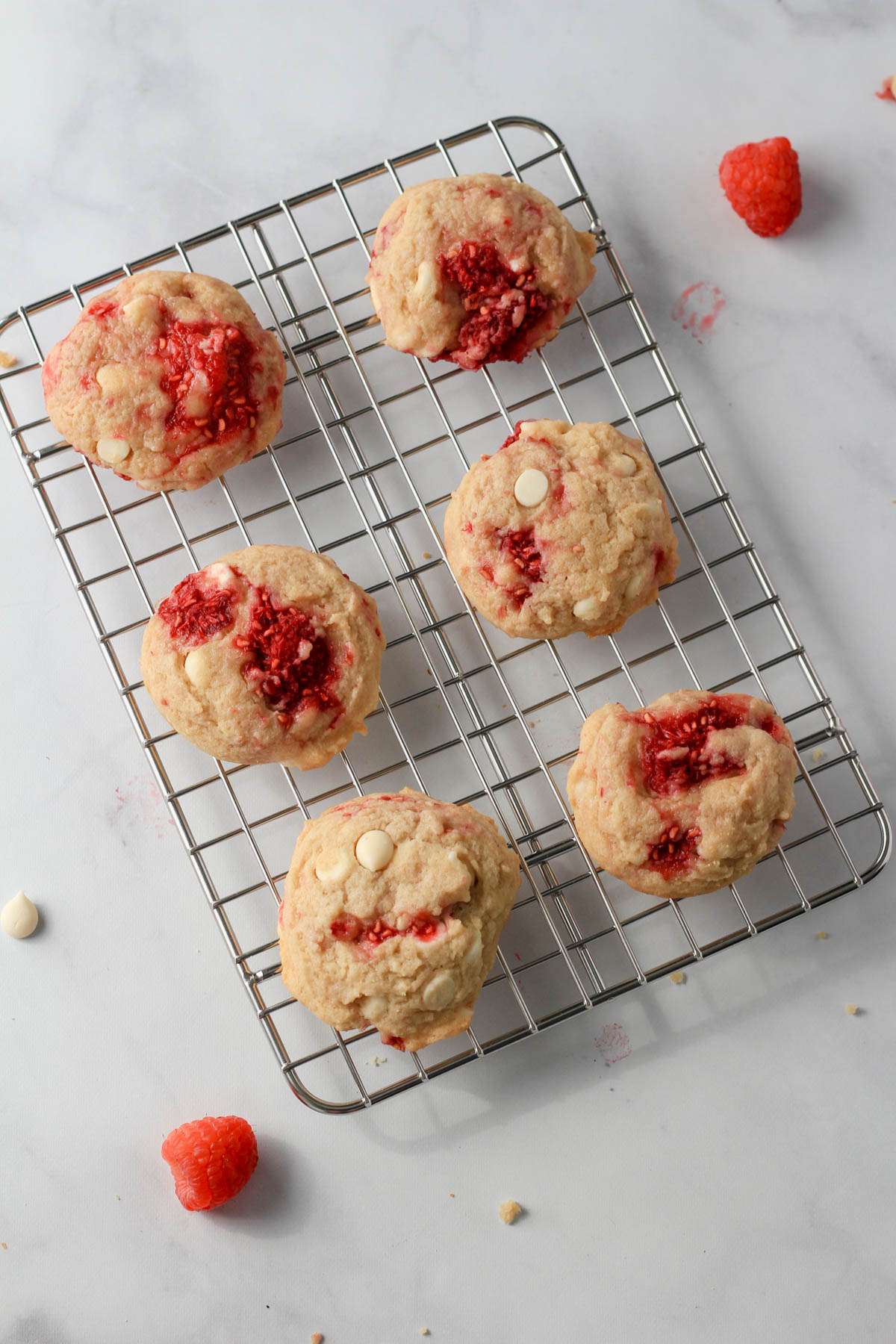 Six dairy-free raspberry white chocolate chip cookies on a cooling rack on a white counter.