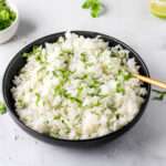 A black bowl filled with vegan cilantro lime rice and a gold spoon on the right side.