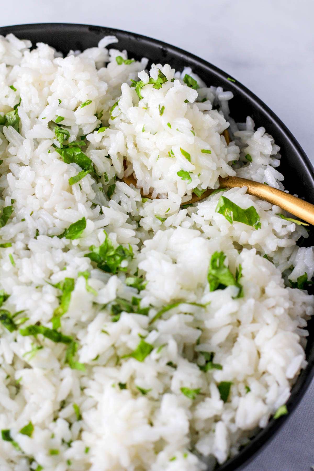 Fluffy cilantro lime rice in a black bowl on top of a gold spoon.