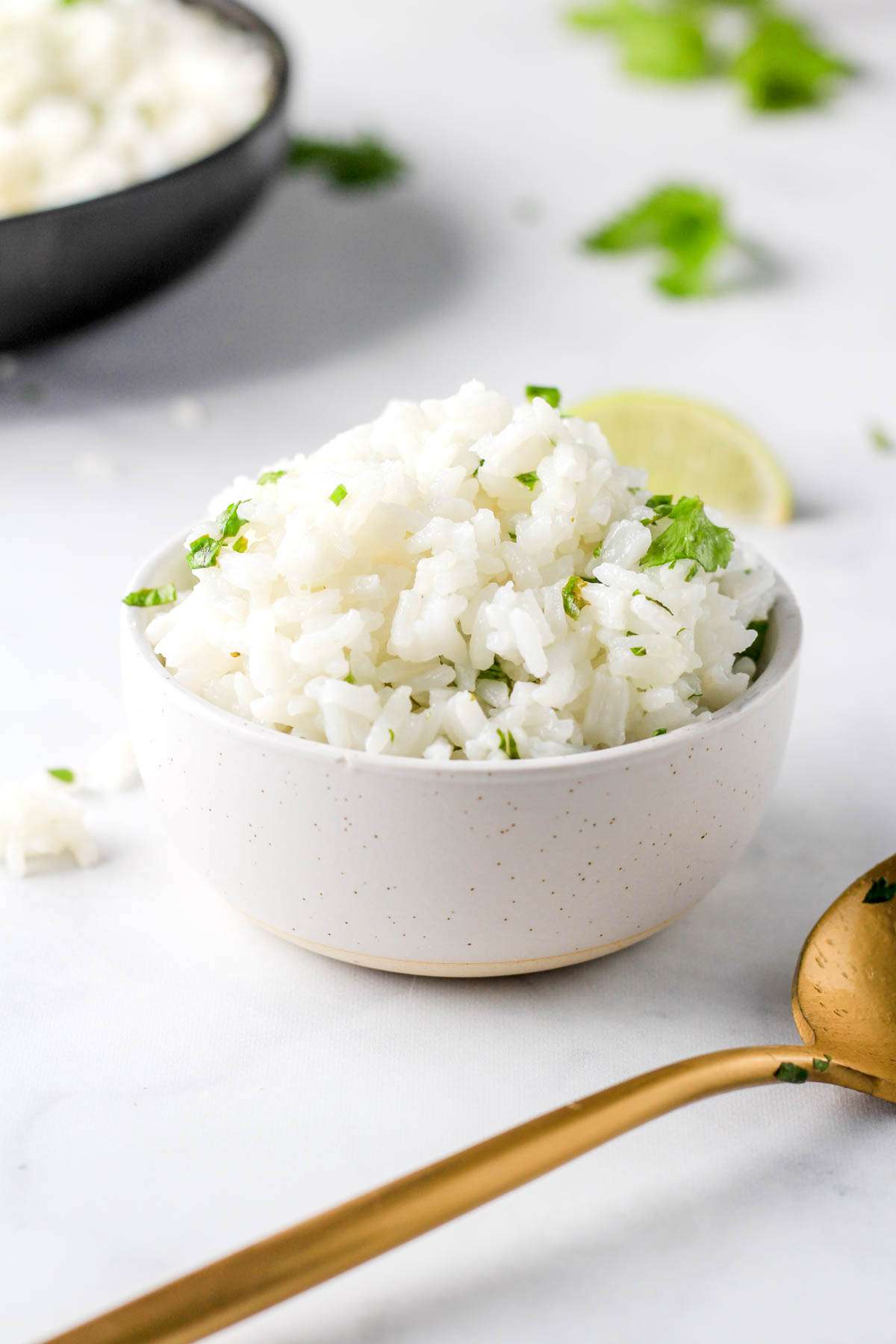 A white bowl filled to the top with vegan cilantro lime rice and a gold spoon on the right side of the counter.