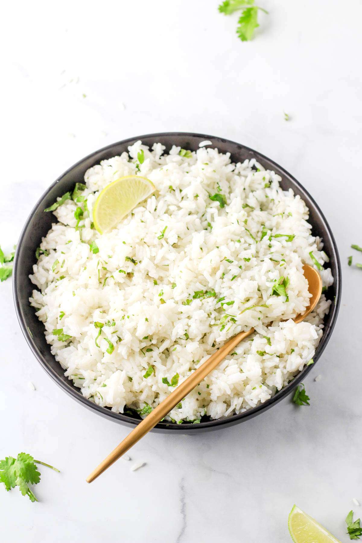 A large black bowl of cilantro lime rice with a gold spoon on the bottom right of the bowl and a lime wedge in the top left.