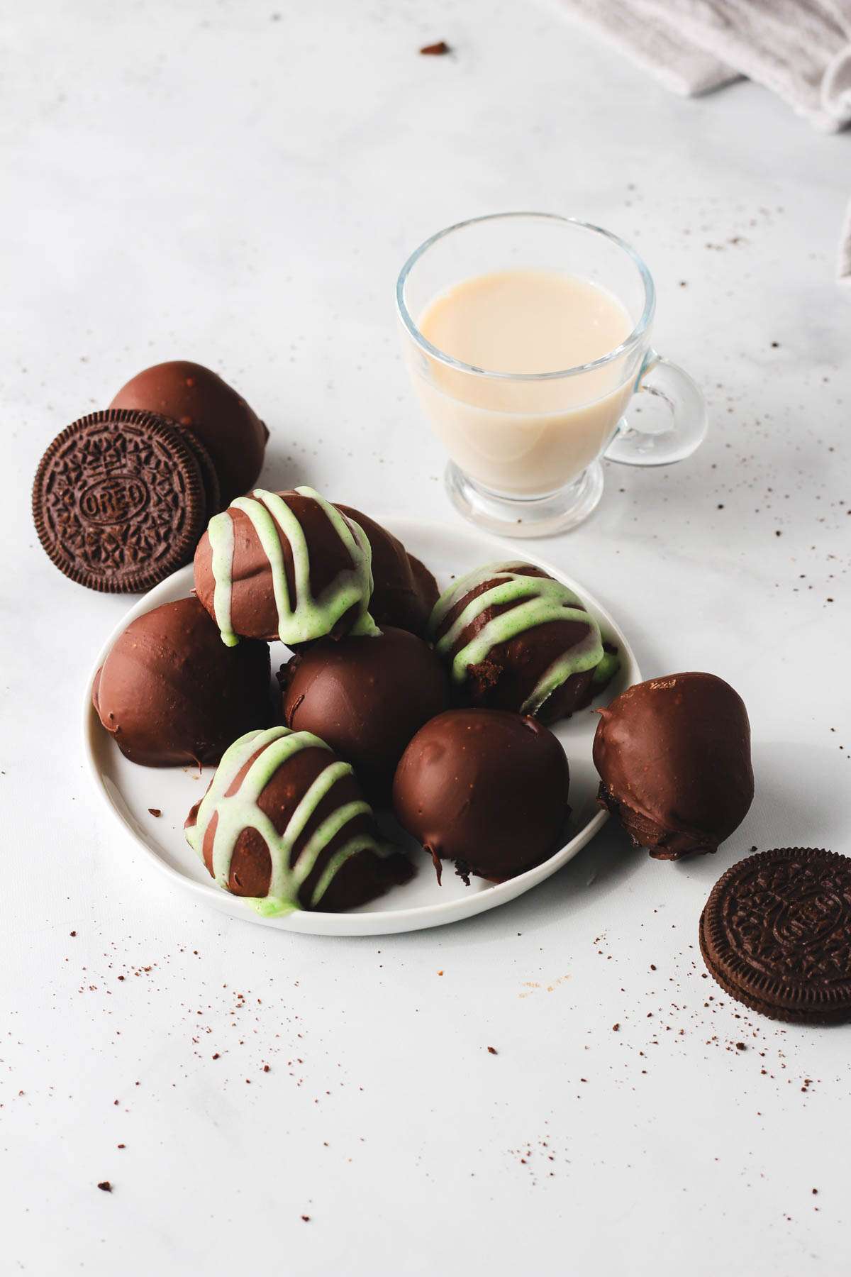 A small plate of Vegan Irish cream Oreo truffles in front of a small glass of Vegan Irish Cream.