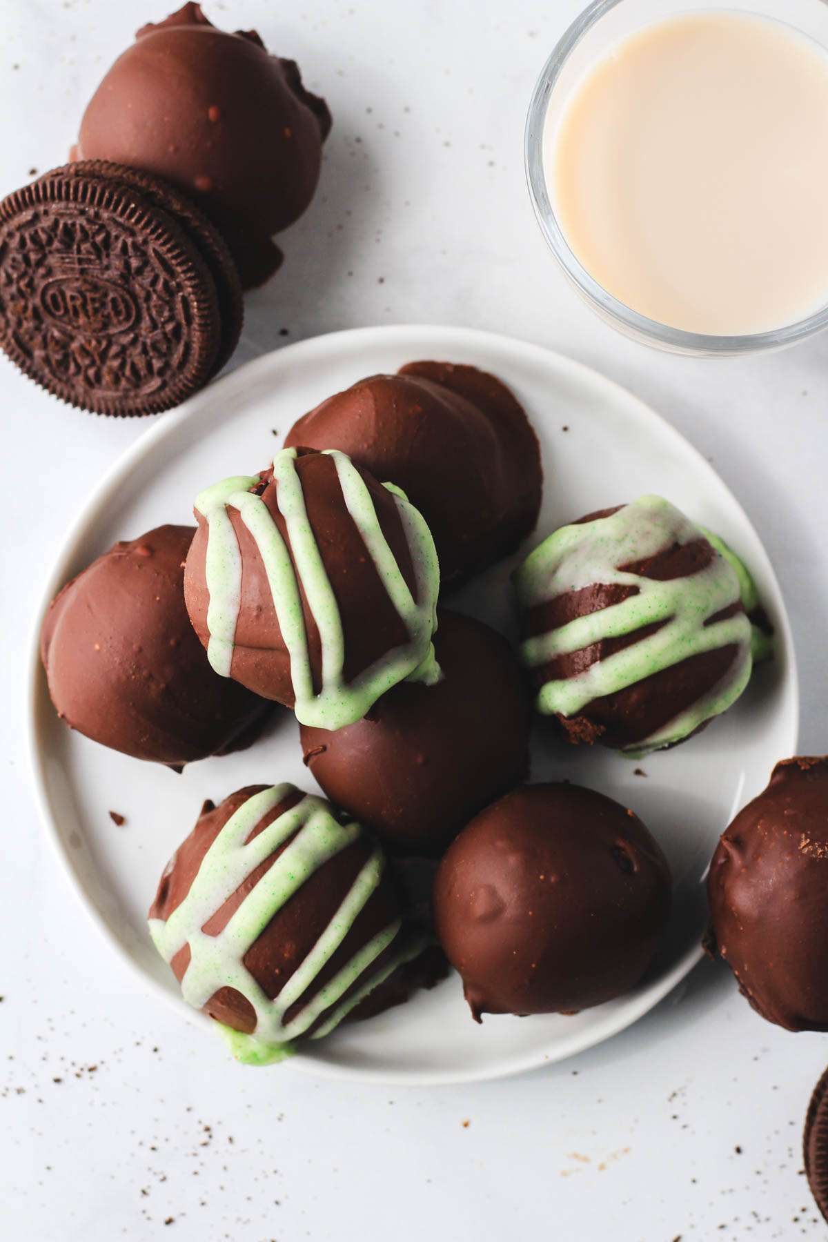 A top down photo of a white plate topped with Irish Cream Oreo truffle balls next to a small glass of vegan Irish cream.