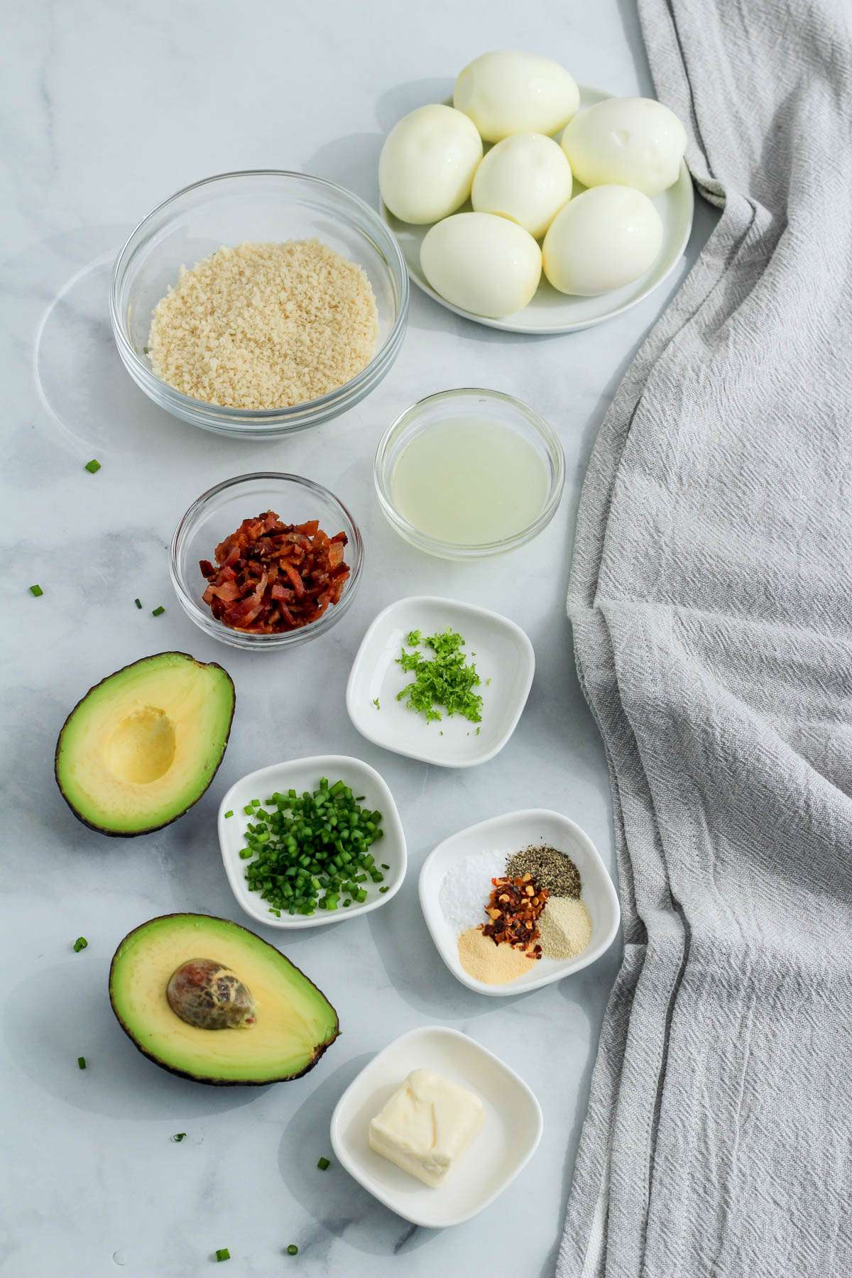 Ingredients for avocado deviled eggs on a white counter with a grey towel.
