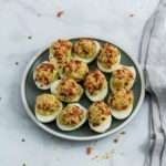 A top down picture of avocado deviled eggs on a green plate on a white counter.