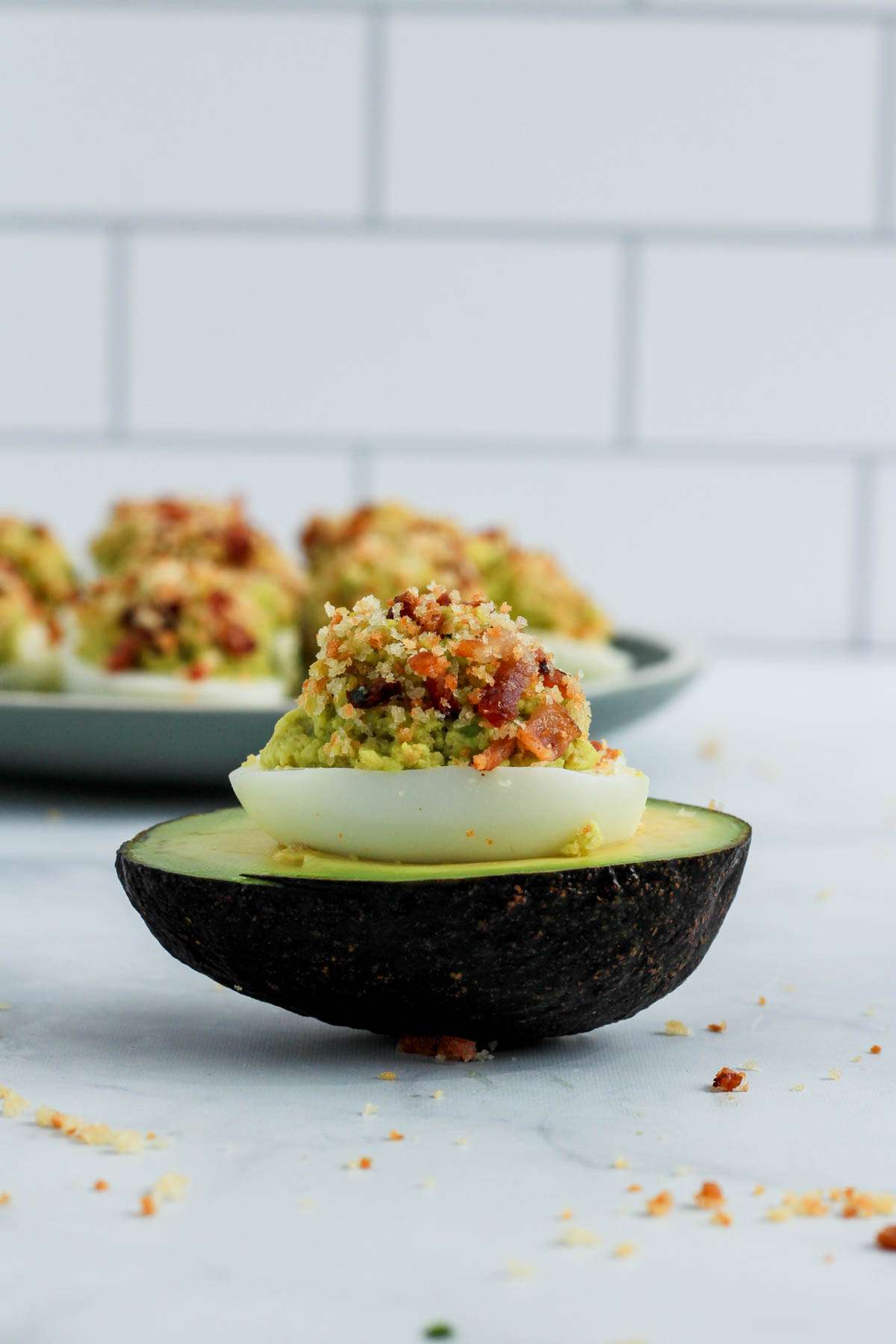 An avocado deviled egg nestled into an avocado half on a white counter.