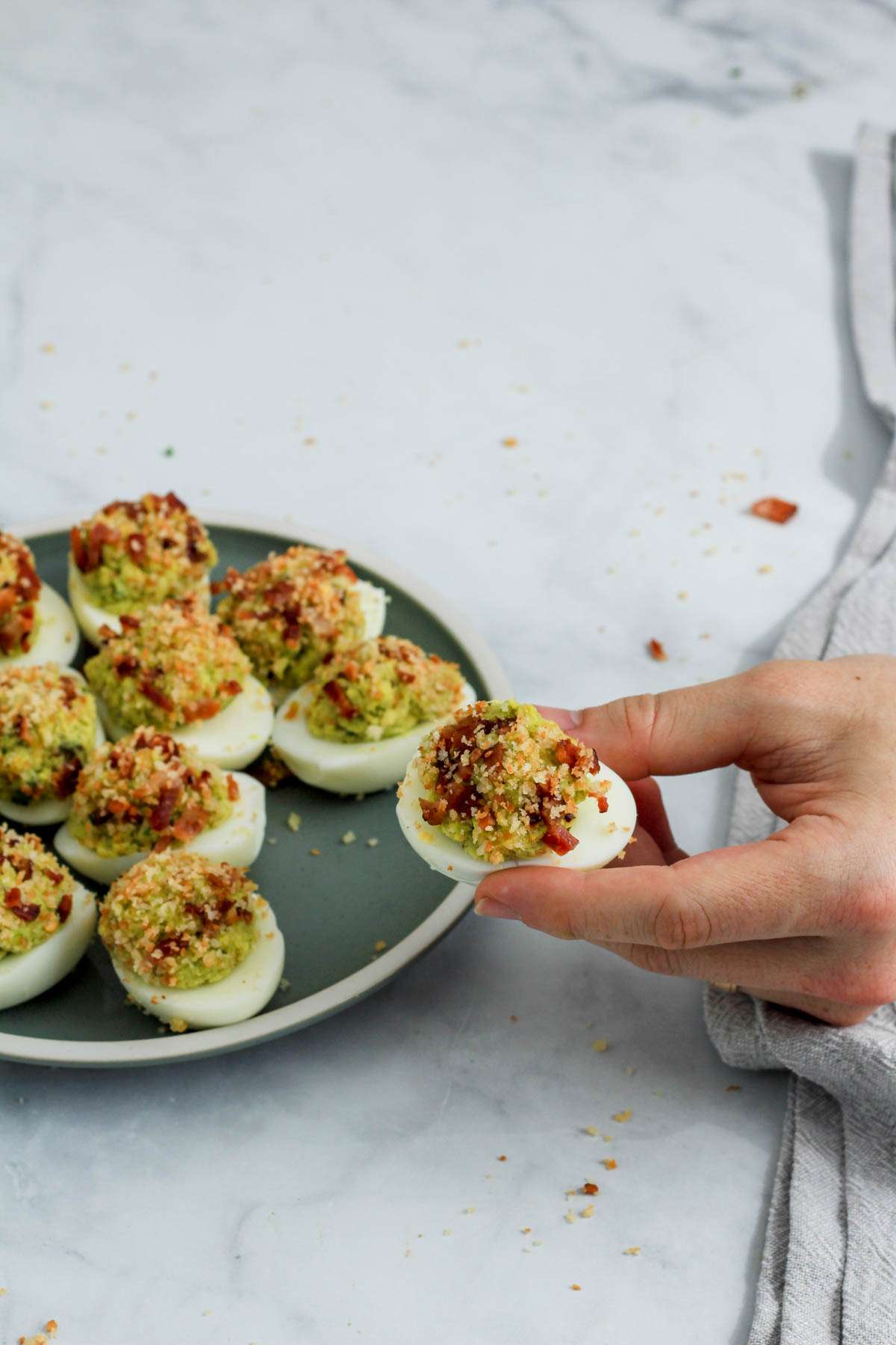 A hand holding an avocado deviled egg in front of a green plate filled with avocado deviled eggs.