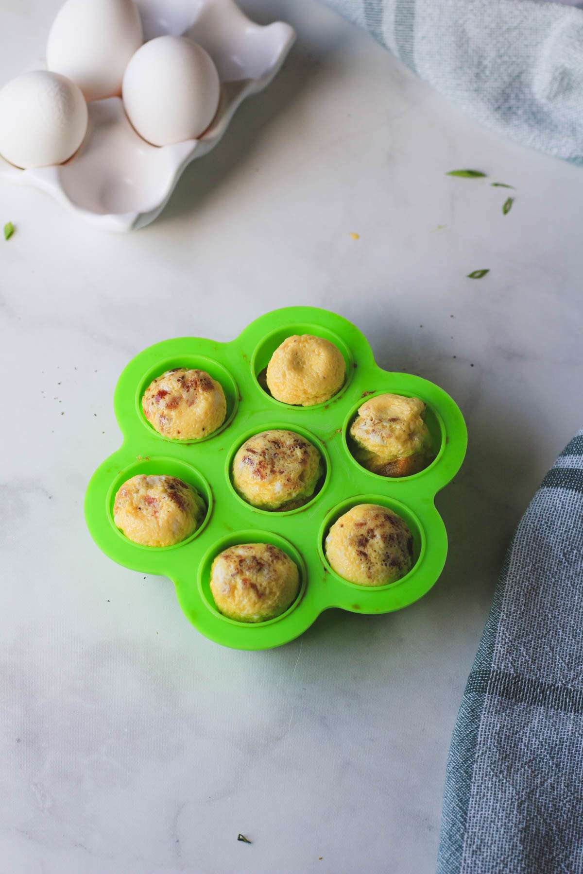 A green egg bite mold with 7 dairy-free egg bites after cooking and being turned over.