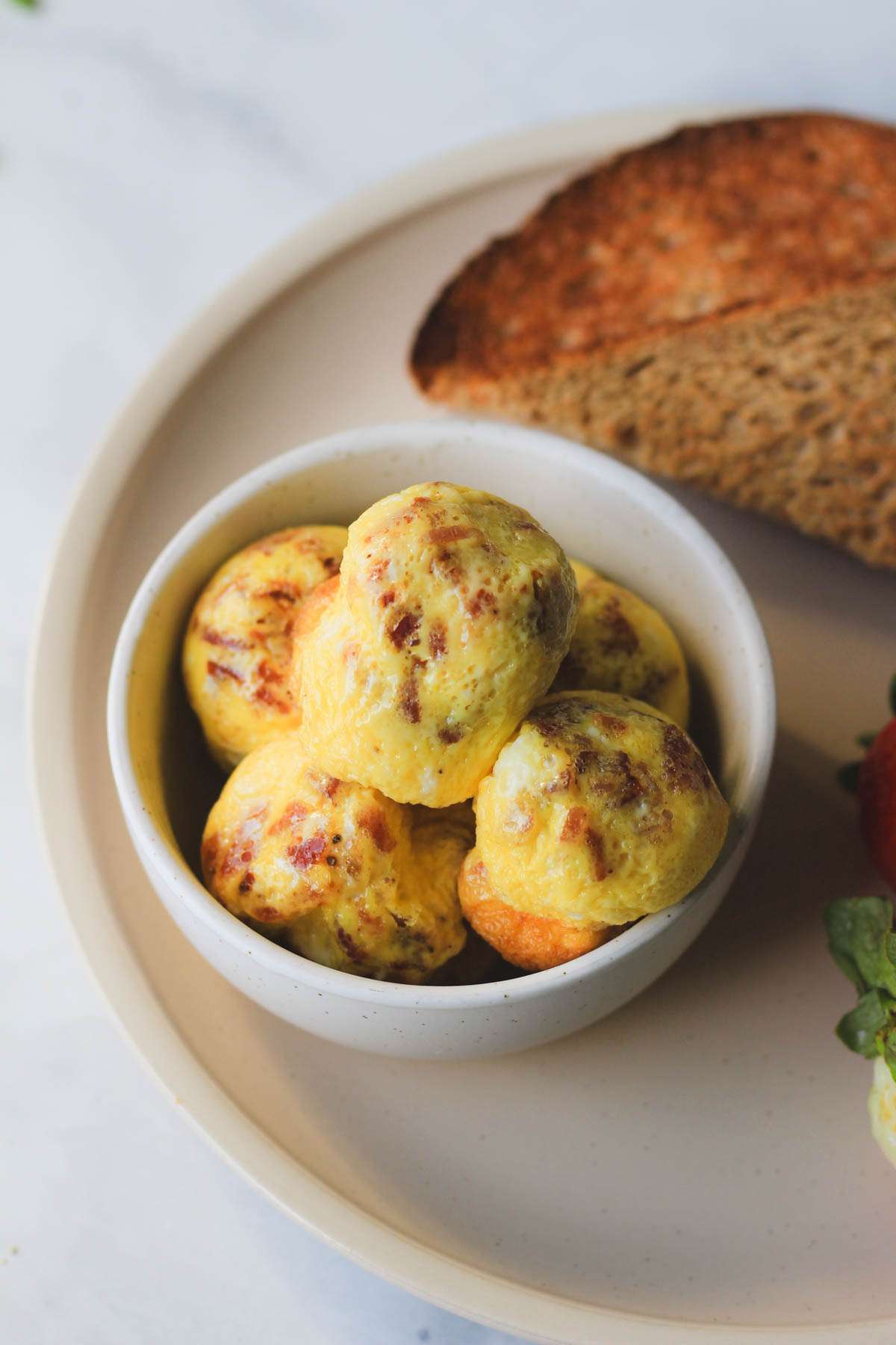 A small white bowl filled with dairy-free egg bites on a cream plate.