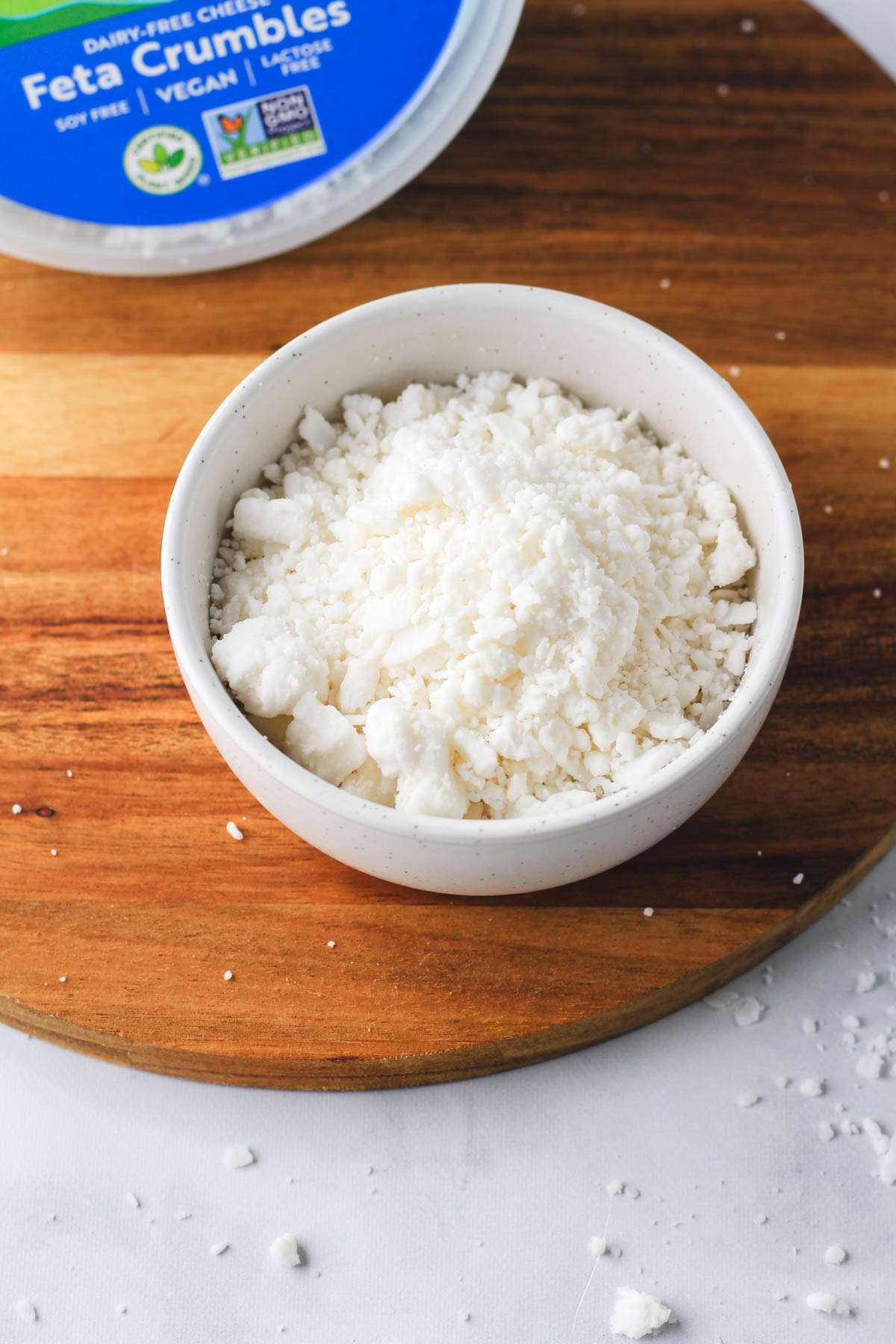 A wooden counter with a white bowl filled with follow your heart feta cheese crumbles.