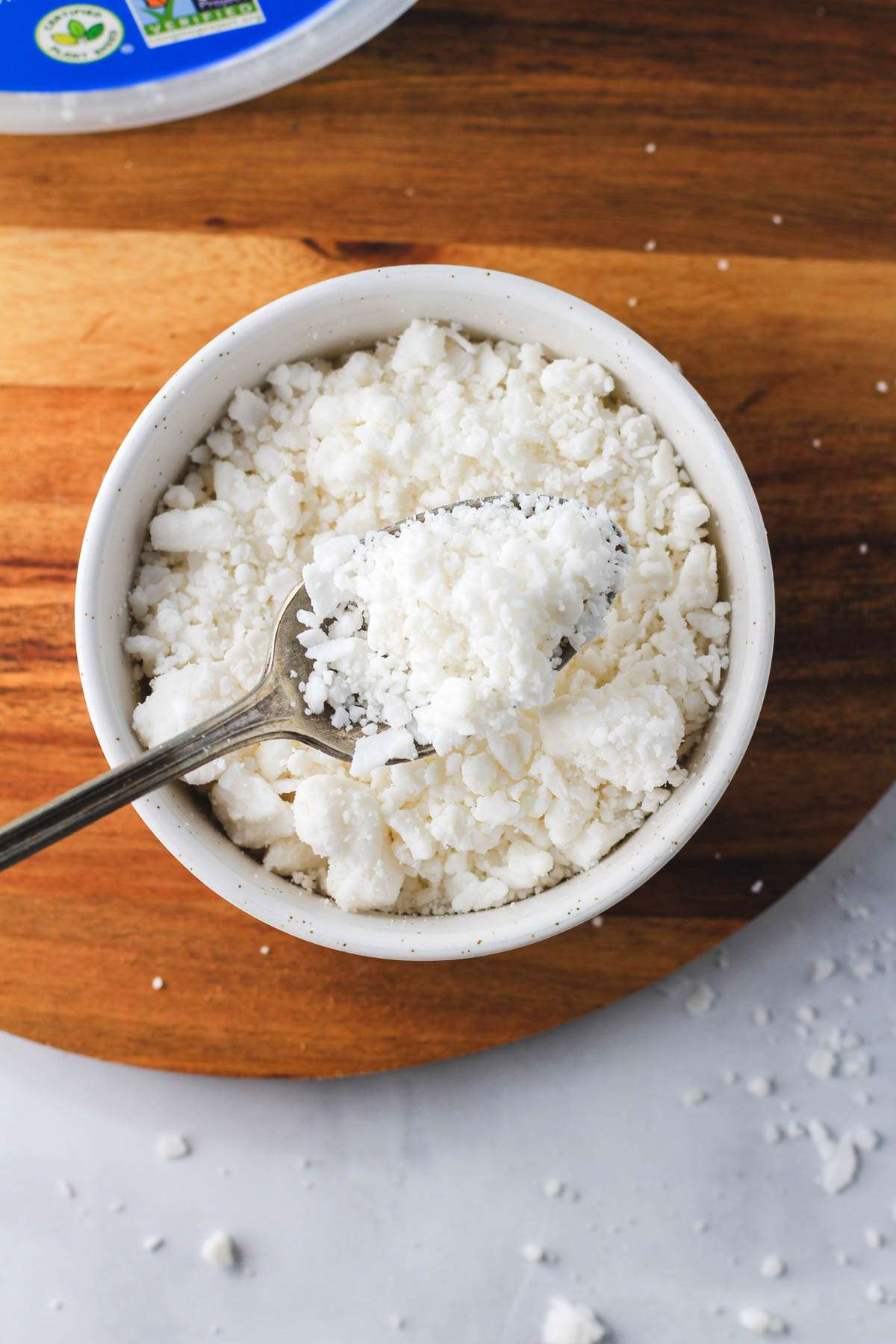 A spoonful of dairy-free feta cheese crumbles over a white bowl of Follow Your Heart Feta cheese.