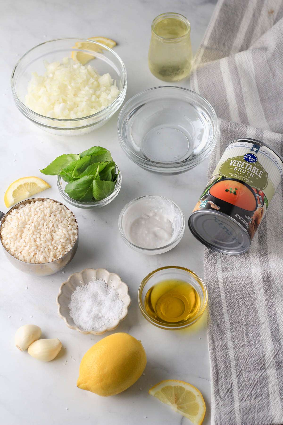 Ingredients for vegan lemon basil risotto on a white counter with a grey and white dish towel.