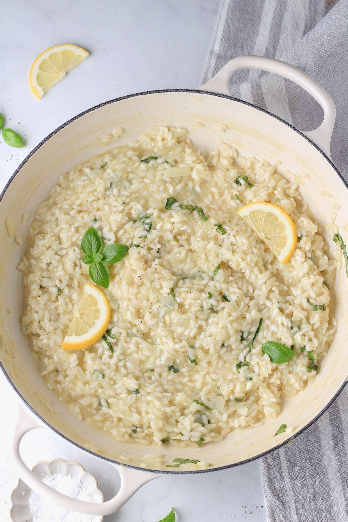 Vegan lemon basil risotto in a white two handled skillet topped with fresh lemon slices and basil leaves.