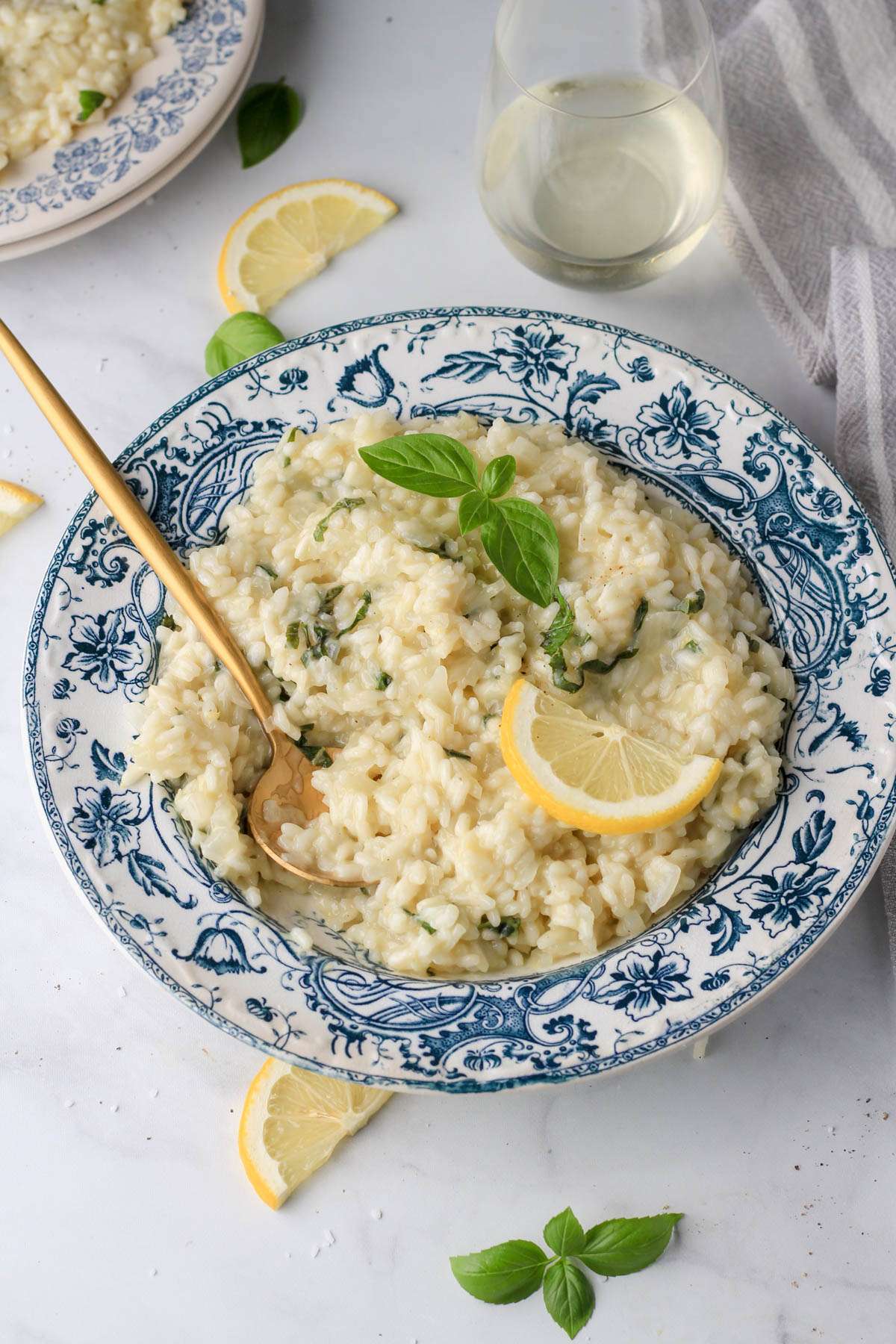 A white and blue rimmed bowl of lemon basil risotto with a gold spoon in the risotto on the left and a wedge of lemon on the right.