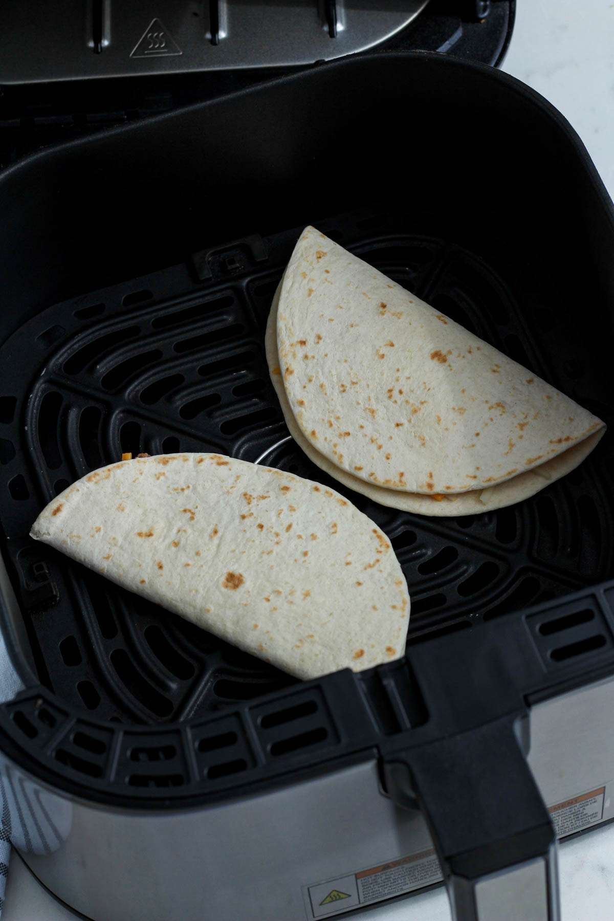 Two flour tortillas in an air fryer before cooking.