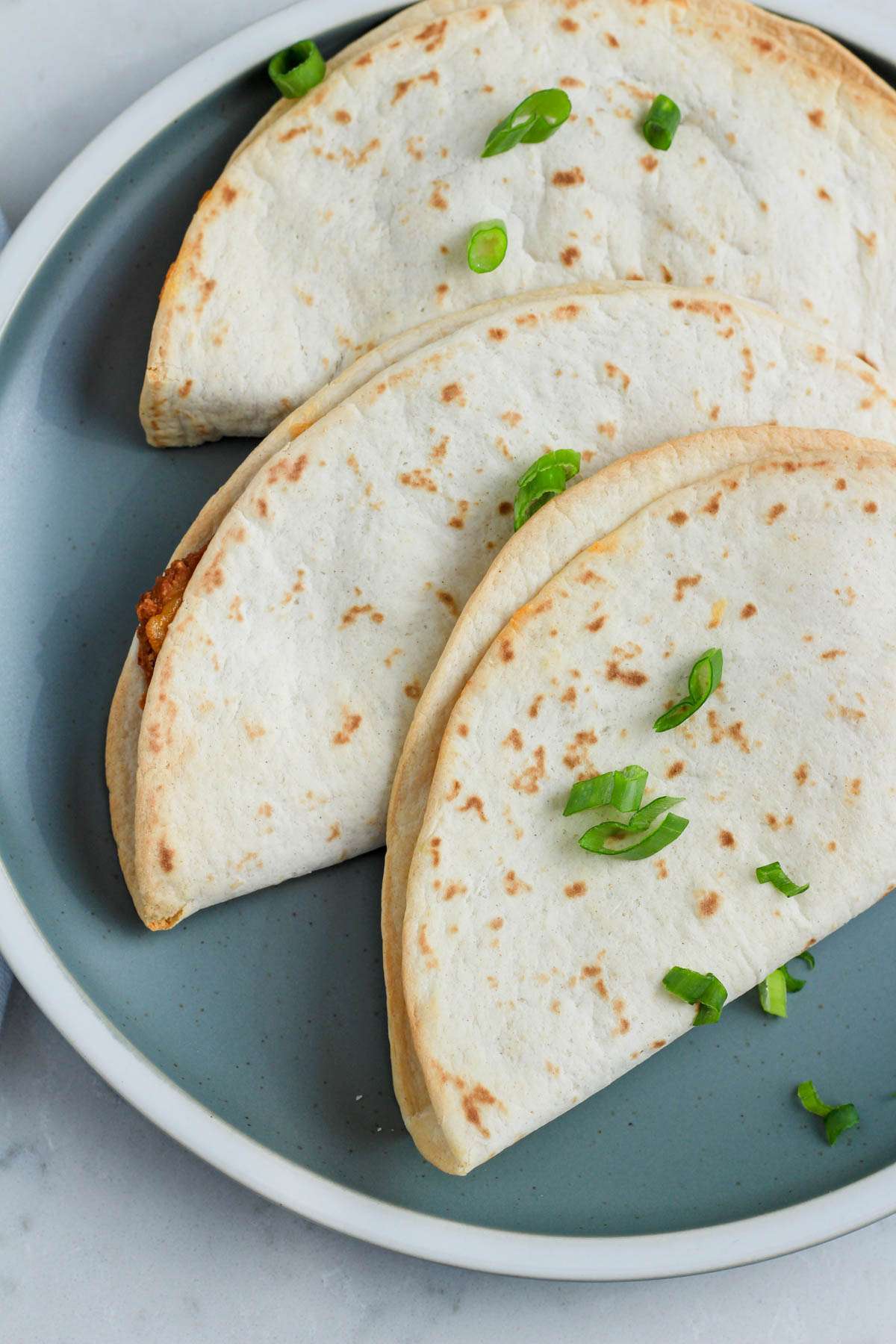 A green plate with crispy air fryer quesadillas topped with green onion.