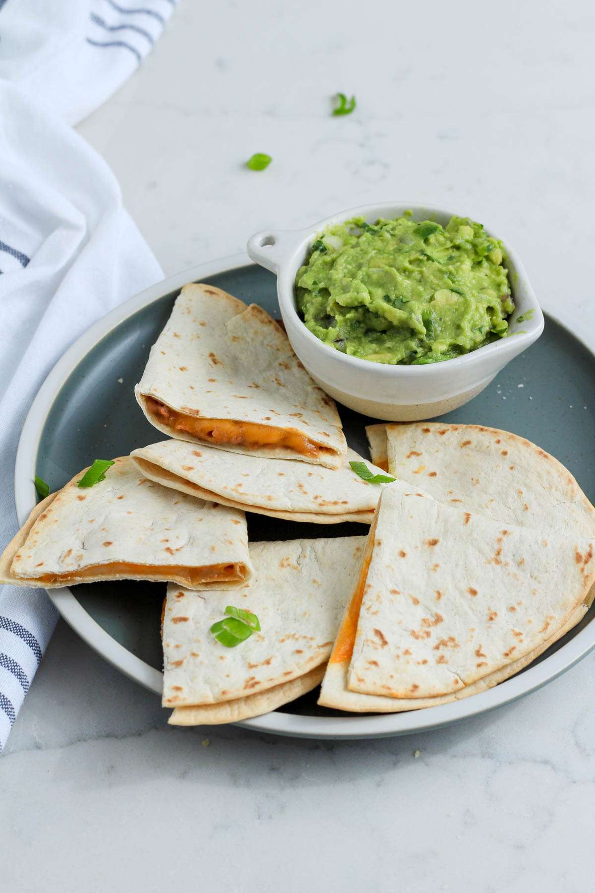 Slices of air fryer quesadillas on a green plate with a small bowl of guacamole on the back side of the plate.