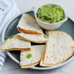 Air fryer quesadillas on a green plate with a small bowl of guacamole.