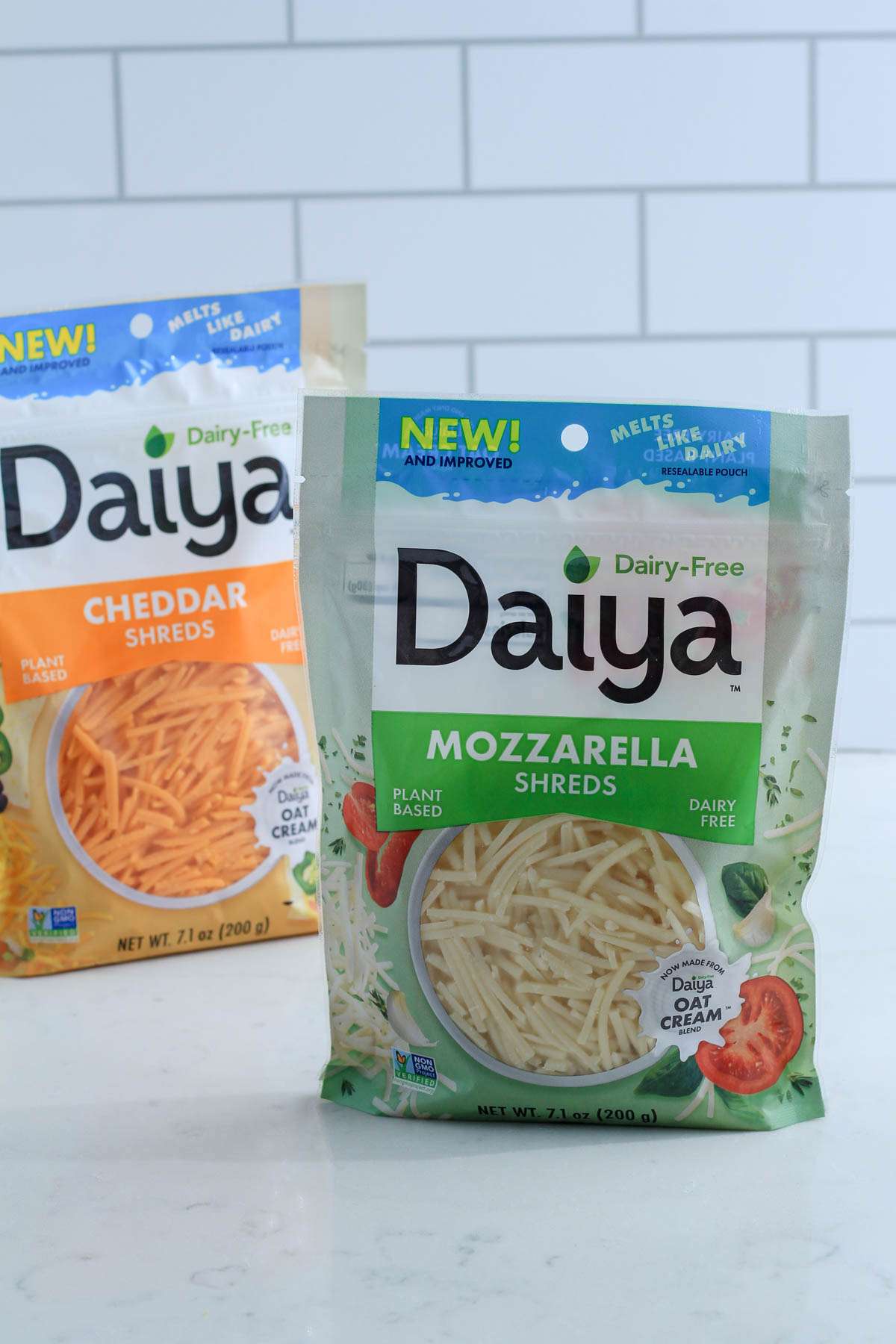 A bag of Daiya Mozzarella Shreds on a white counter in front of a bag of cheddar shreds.