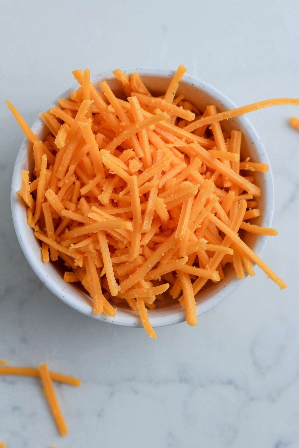 A small white bowl filled with Daiya Cheddar Cheese on a white counter.