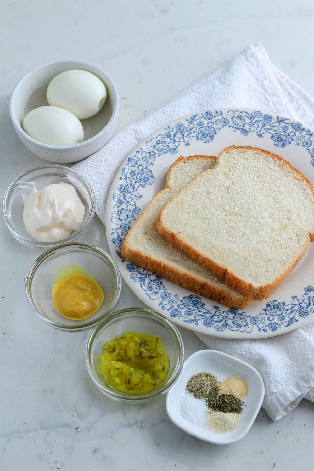 A white counter with ingredients for dill pickle egg salad sandwiches.