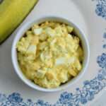 A close up of a small white bowl with dill pickle egg salad on a white and blue plate.