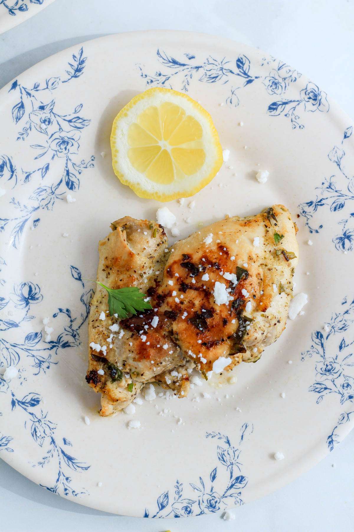 A top down photo of a marinated chicken thigh with feta and lemon.