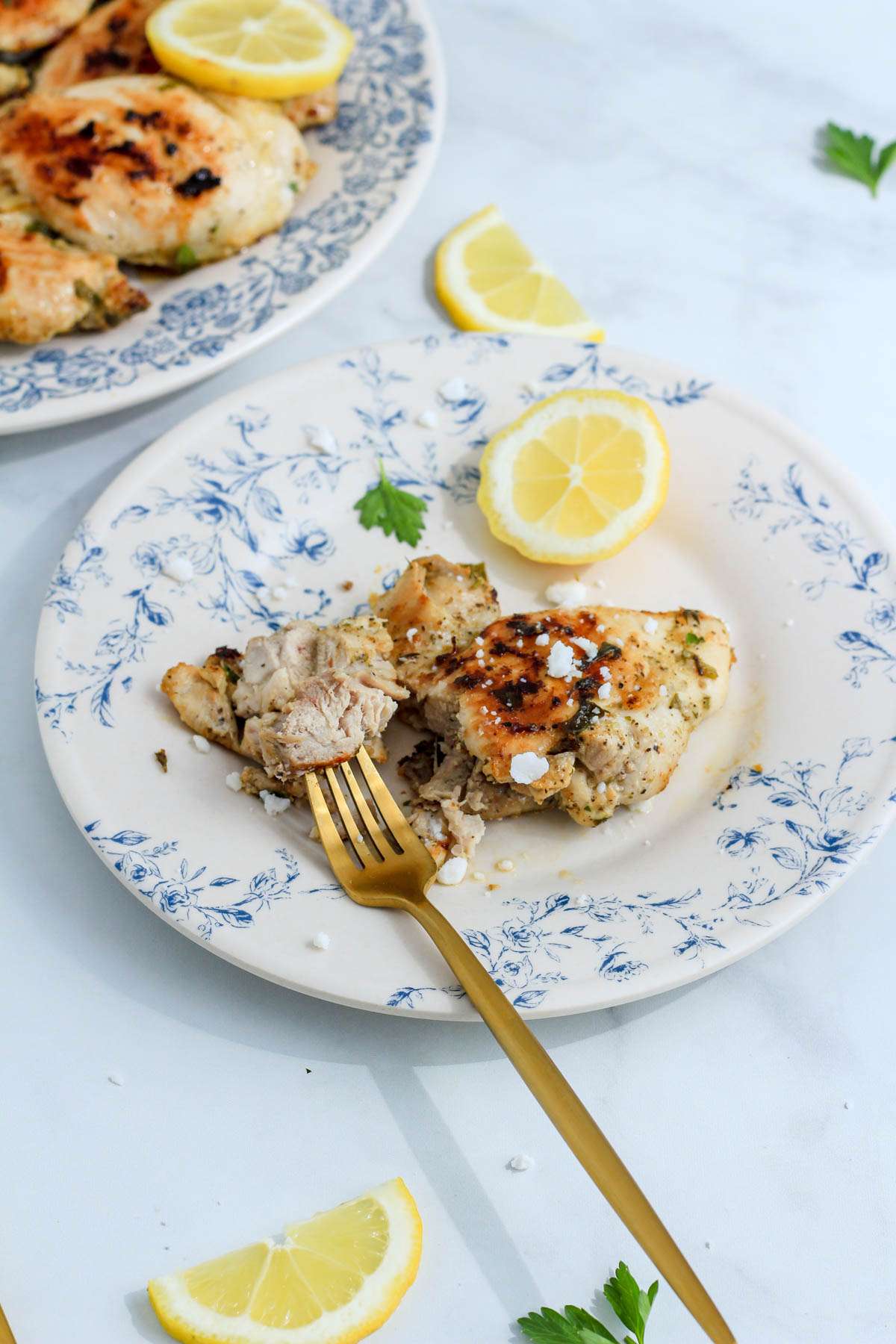 A Greek chicken thigh with a gold fork on a white and blue plate.