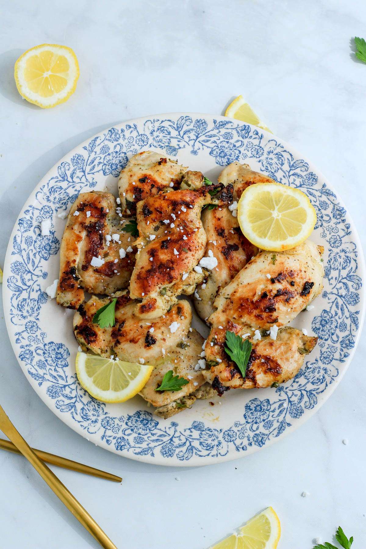 A white and blue plate on a white counter topped with Greek marinated chicken thighs.